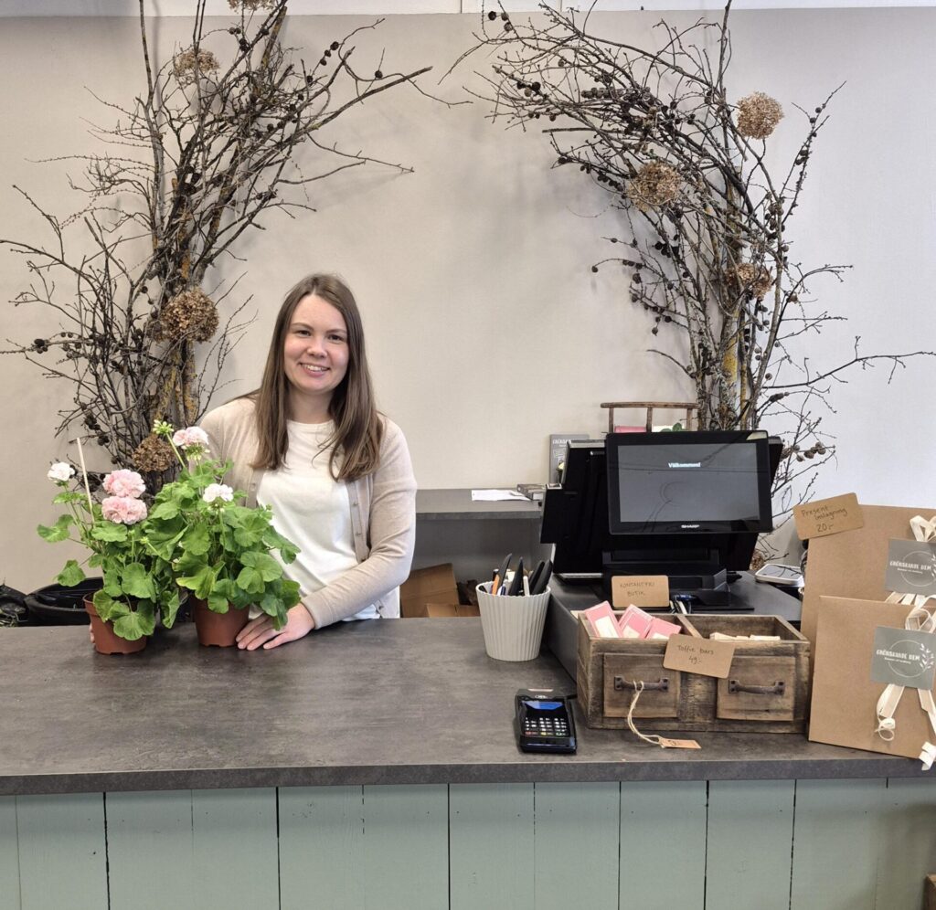 Referenskund som är Grönskande Hem i Borlänge. Butikchef Rebecka står med blommor bredvid kassasystem från oss.